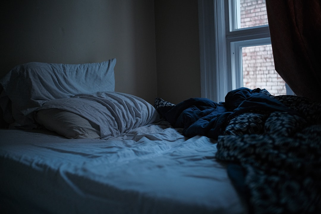 An unmade bed in a dark, quiet bedroom.