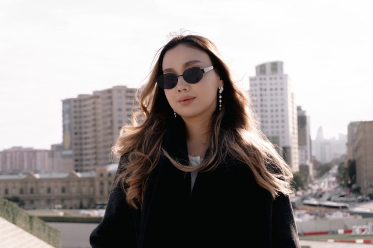 Stylish woman wearing sunglasses with city buildings behind.