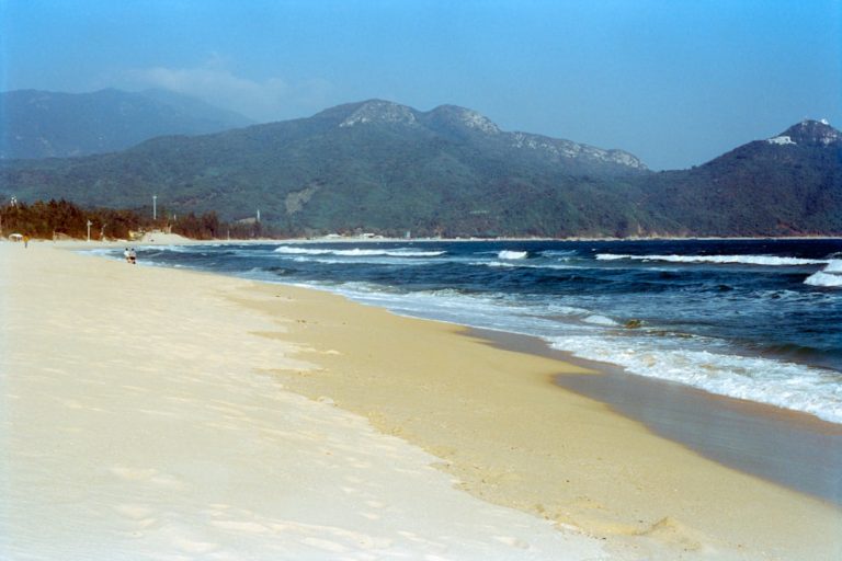 Sandy beach with blue ocean waves and mountains.