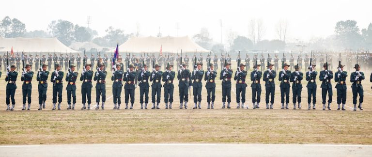 Soldiers in uniform stand at attention with rifles.