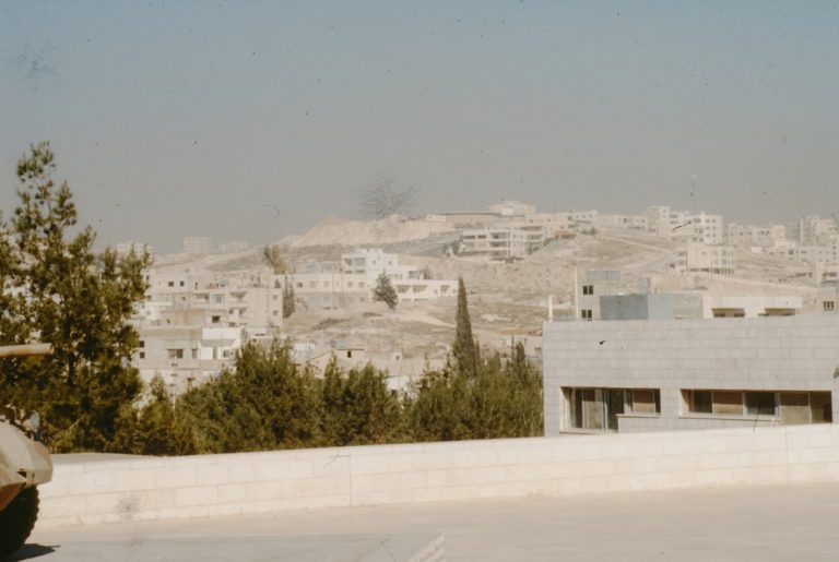 Buildings on a dusty, arid hillside under a hazy sky.