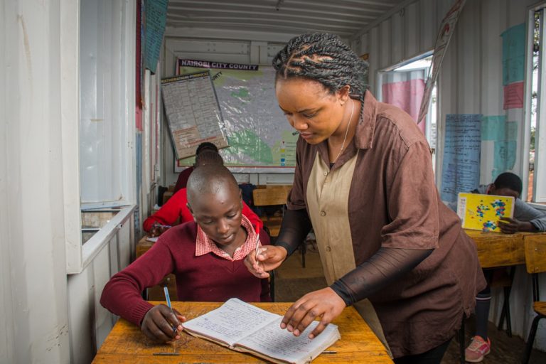 A teacher assists a student in a classroom.