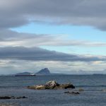 A cargo ship sails past a rocky outcrop at sea.